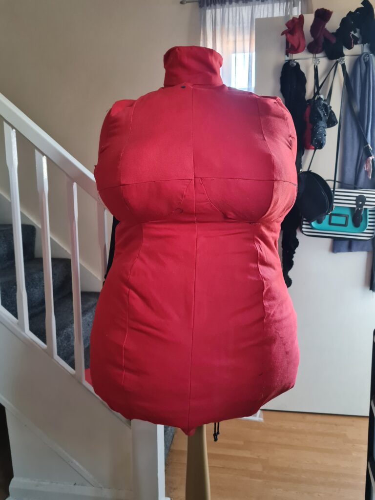 A red plus-size dress form standing at the bottom of a staircase